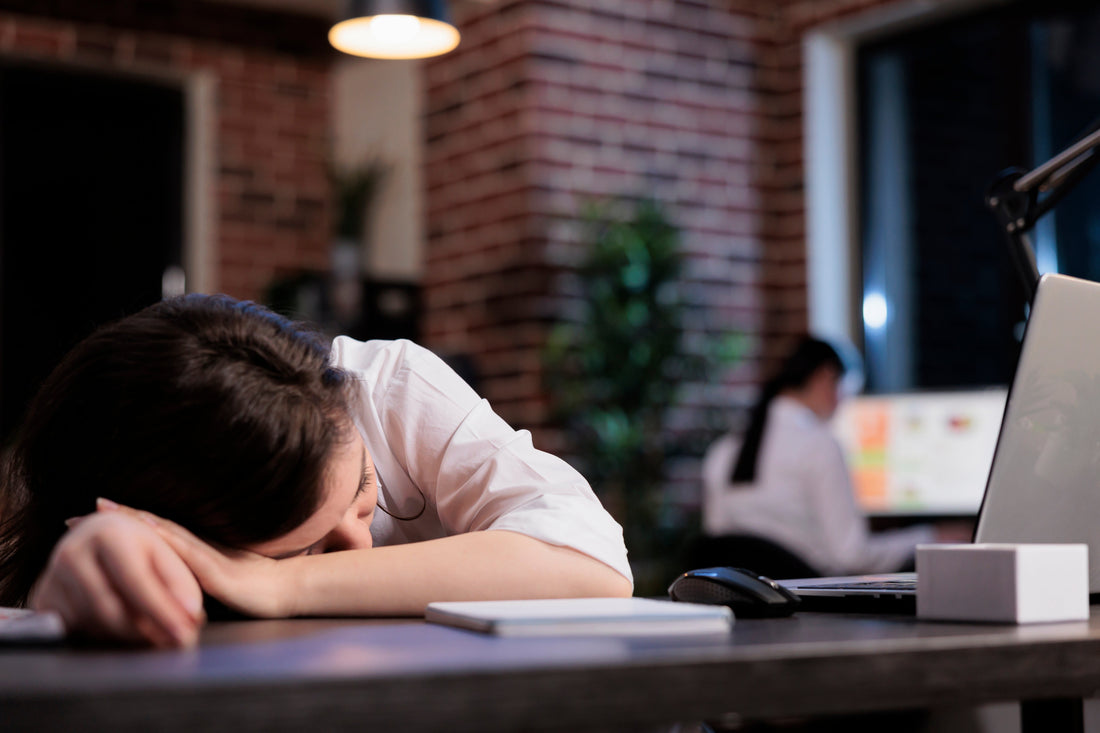 Femme fatiguée qui ne prend pas de magnésium et qui s'endort au travail sur son bureau.