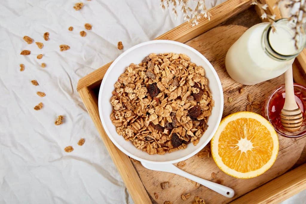 Petit-déjeuner sain et équilibré pour un moral d’acier, composé de céréales complètes sous forme dem uesli, d'une demie orange, de miel et de lait, apporté au lit