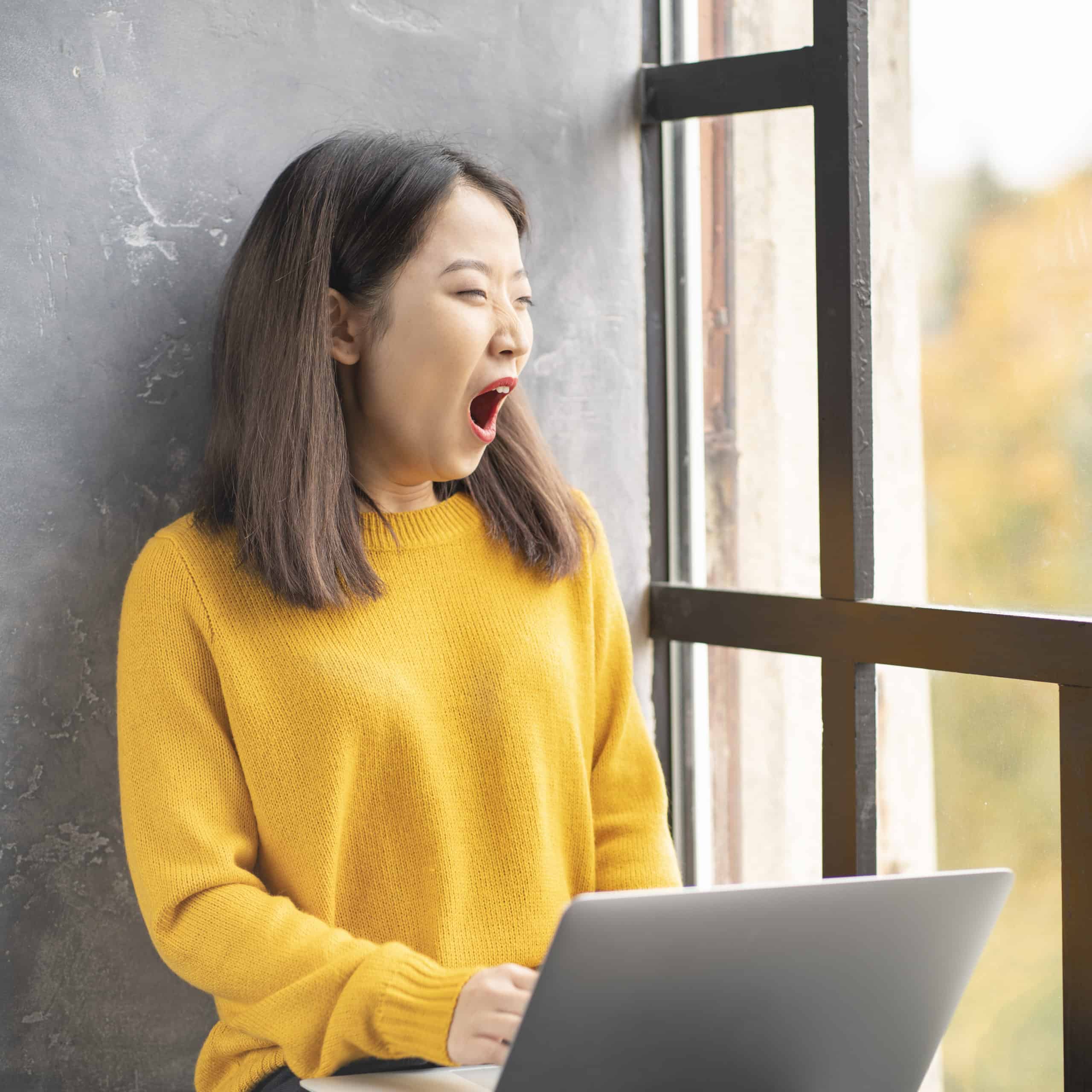jeune femme souffrant de fatigue intense, en train de bâiller devant son ordinateur