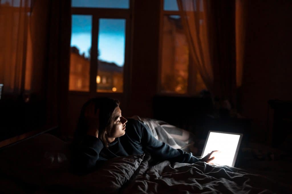 Femme allongée dans la pénombre devant la lumière bleue de sa tablette