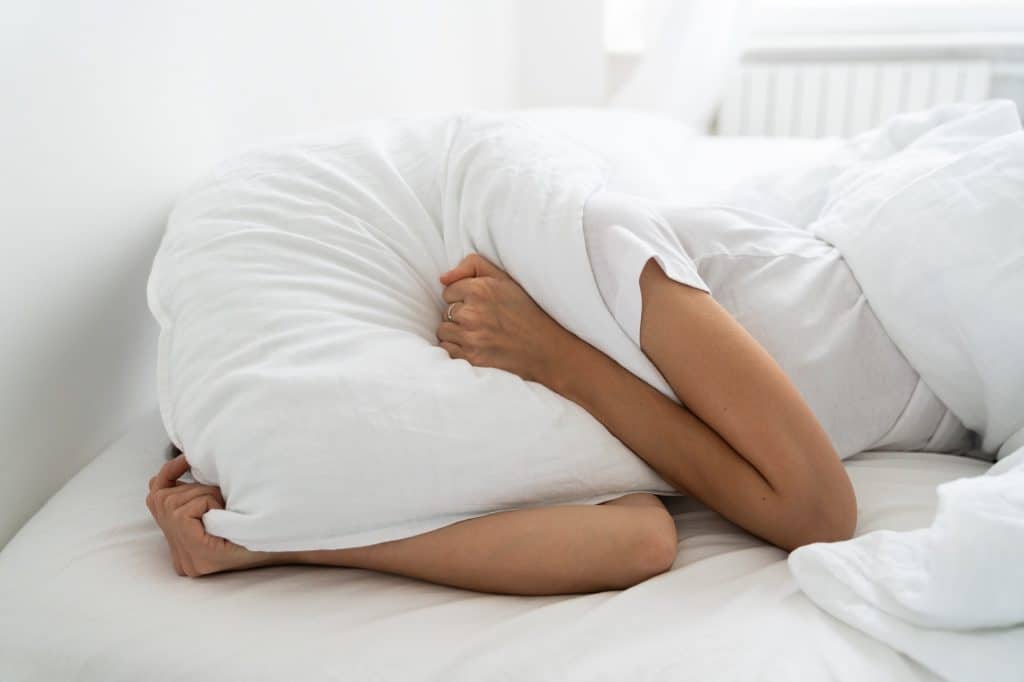 Cette femme, manquant de sommeil, se couvre le visage avec son oreiller dans son lit