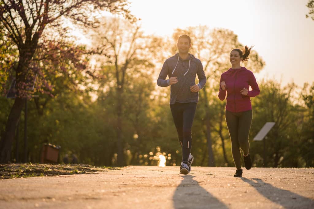 Pratiquez une activité physique pour booster votre système immunitaire, comme ce joyeux couple qui fait du jogging dans un parc par un après-midi ensoleillé