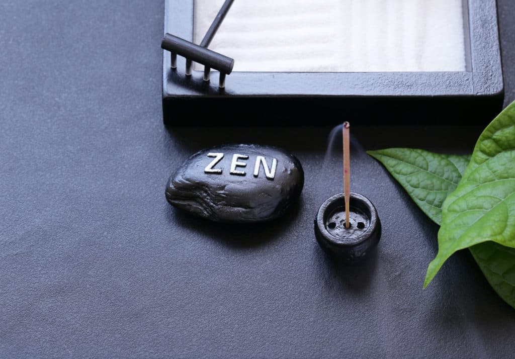 Une pierre avec le mot Zen inscrit dessus, entouré d'encens et d'un mini jardin japonais relaxant